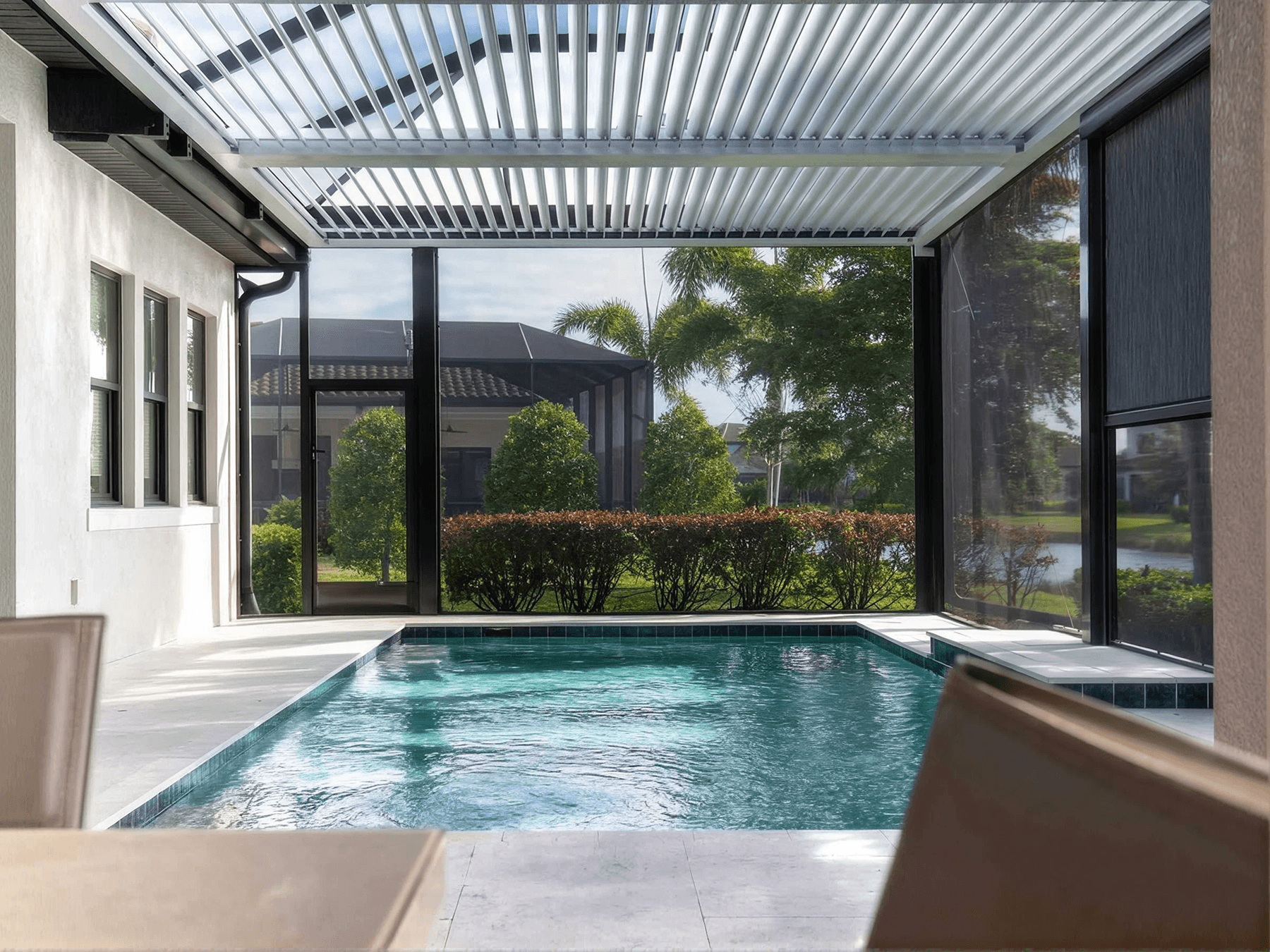 Modern screened patio with a shimmering pool, surrounded by lush greenery. The setting is serene and inviting, with a sleek, open pergola roof.