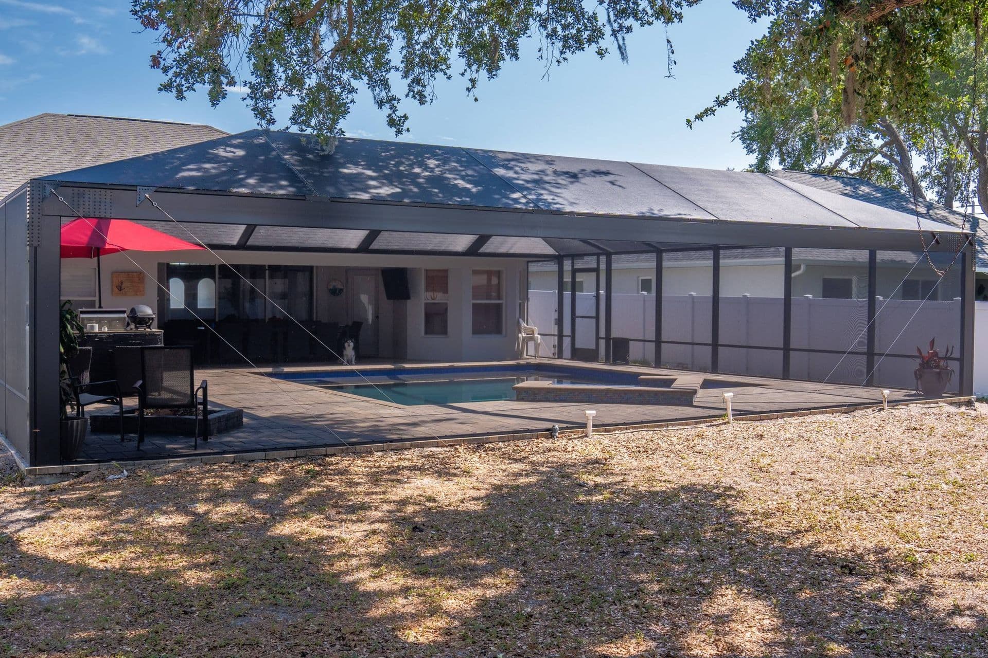 Screened pool enclosure with an Absoview front wall over swimming pool and spa on paved deck, attached to residential home with red umbrella and outdoor seating area.