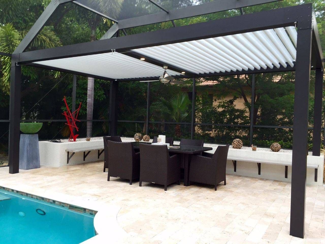 Modern outdoor patio with a black pergola, white louvered roof, dining table and chairs beside a turquoise pool, surrounded by lush greenery.
