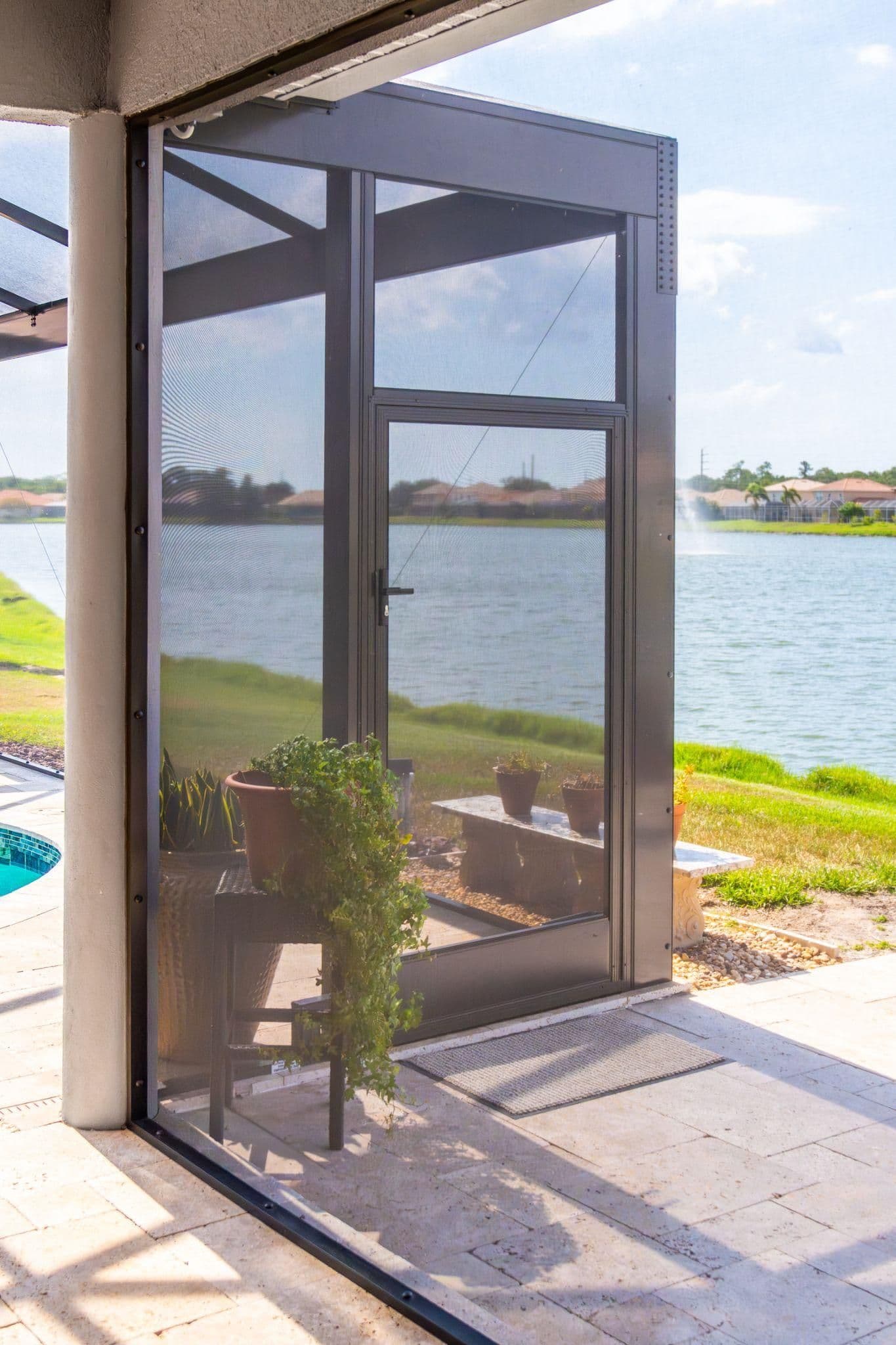 Screened patio and door overlooking a lake and green lawn, with potted plants visible on the patio.