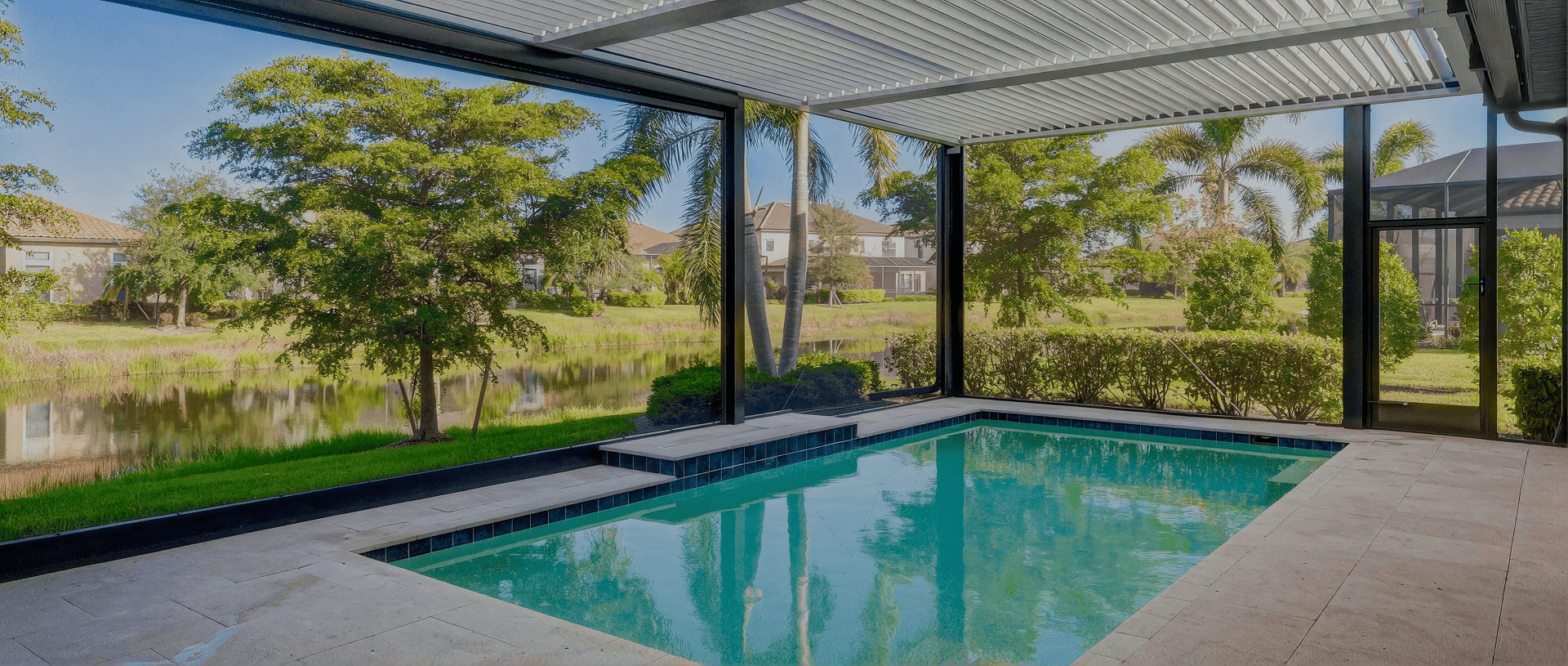 A screened-in pool with a louvered pergola, surrounded by a scenic view of the water.