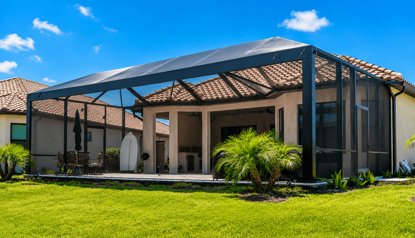 Screened lanai with metal frame and barrel tile roof attached to residential home with tropical landscaping and lawn.