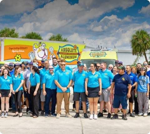 Large group of people wearing blue Absolute Aluminum shirts standing together in front of an Absolute Aluminum building on a sunny day.