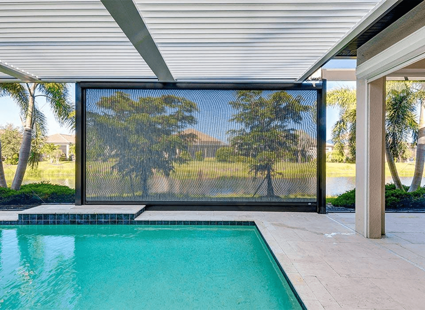 Turquoise backyard pool beneath a covered patio, with screened panels, palm trees, and sunny lawns creating a calm resort-like setting.