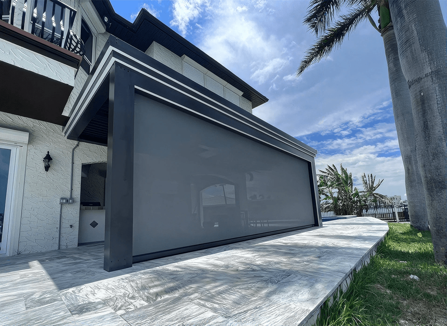 Modern tropical home with a sleek screened patio enclosure, white walls, palm trees, bright blue sky, and a calm, upscale atmosphere.