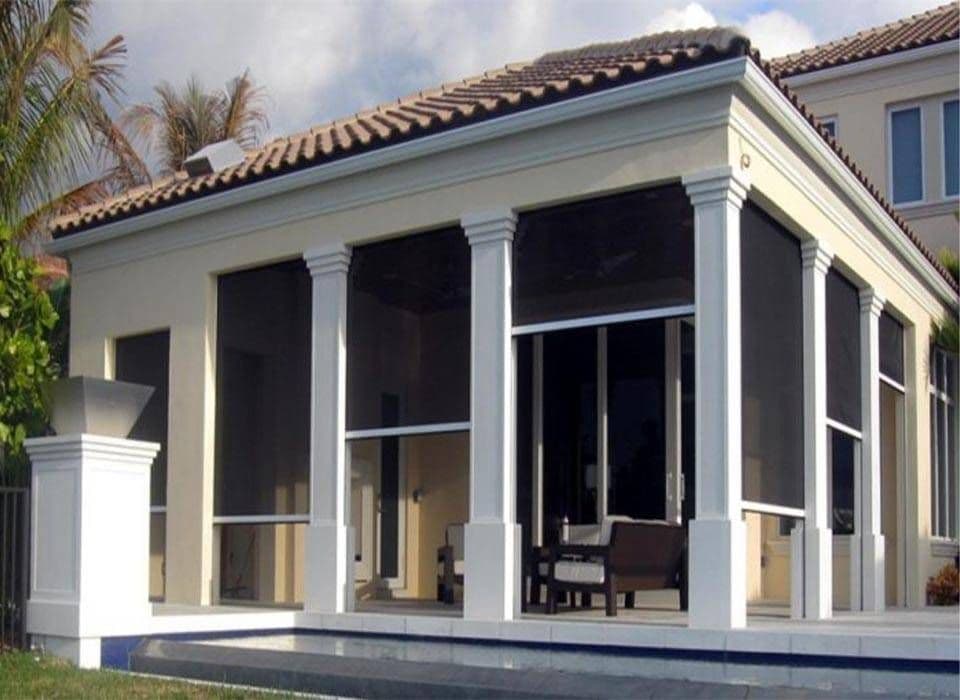 Elegant Mediterranean-style home with white columns, screened porch, tiled roof, palm trees, and outdoor seating in bright sunlight.