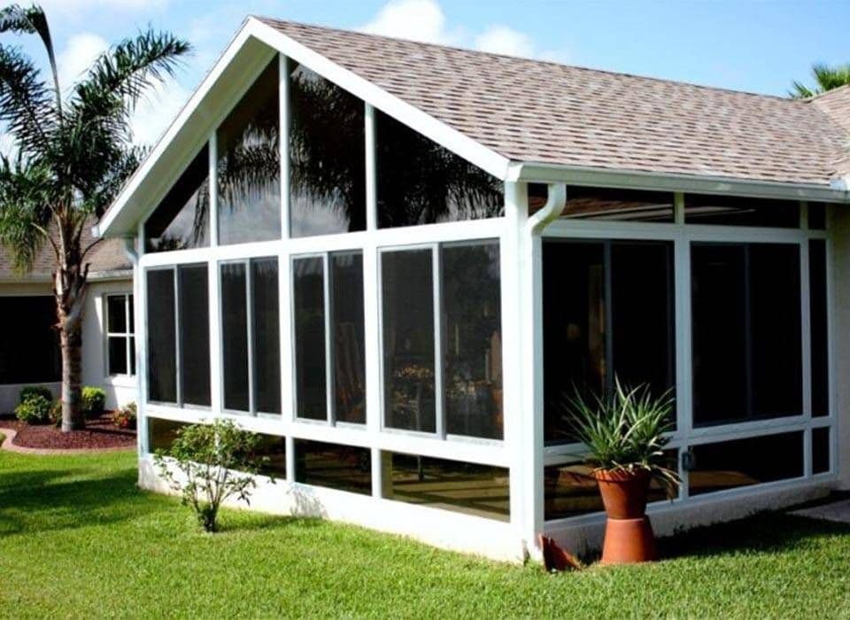 Bright Florida home with a screened-in patio, white framing, glass panels, palm trees, green lawn, and potted plants under a sunny sky.