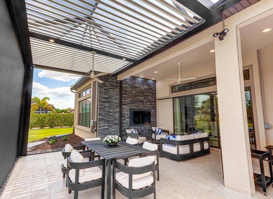 Modern covered outdoor patio with a slatted pergola, dining table and chairs, lounge seating, fireplace, and lush tropical garden views.