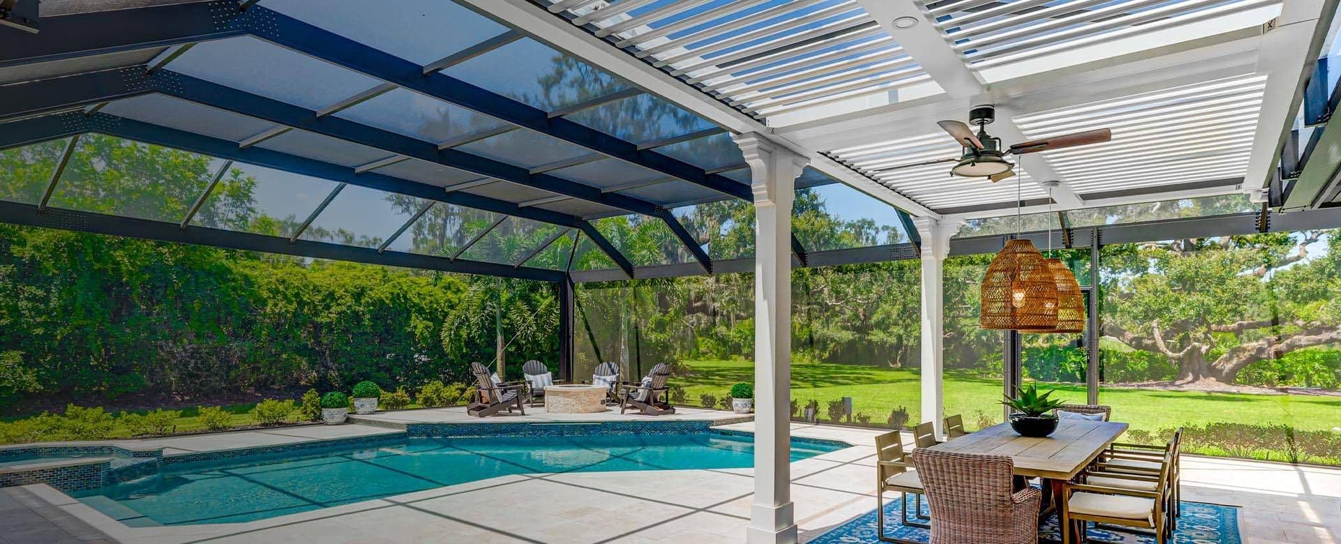 Sunlit covered patio with ceiling fan, wicker dining set, and hanging lamp overlooks a turquoise swimming pool and lush garden, creating a serene retreat.