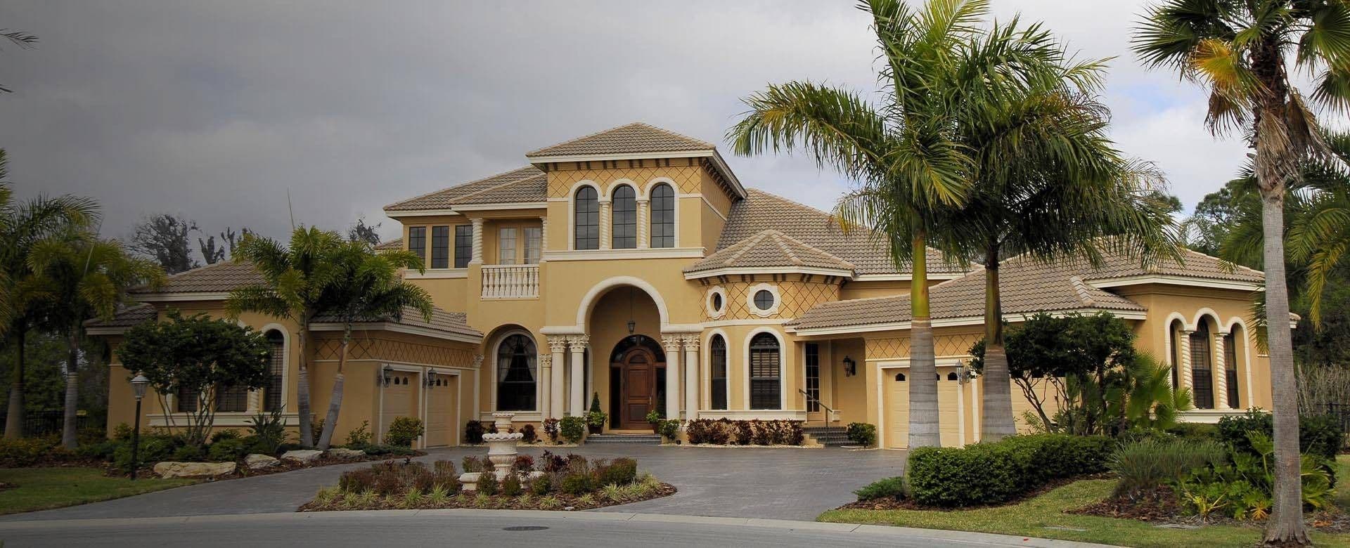 A large home surrounded by palm trees, featuring a spacious driveway leading up to the entrance.