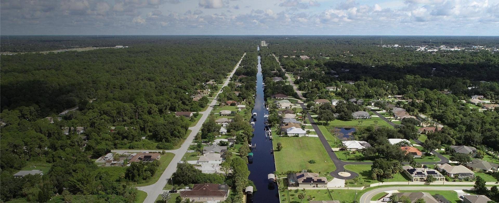 Aerial view of a canal winding through a residential neighborhood, showcasing houses and green spaces along the water.