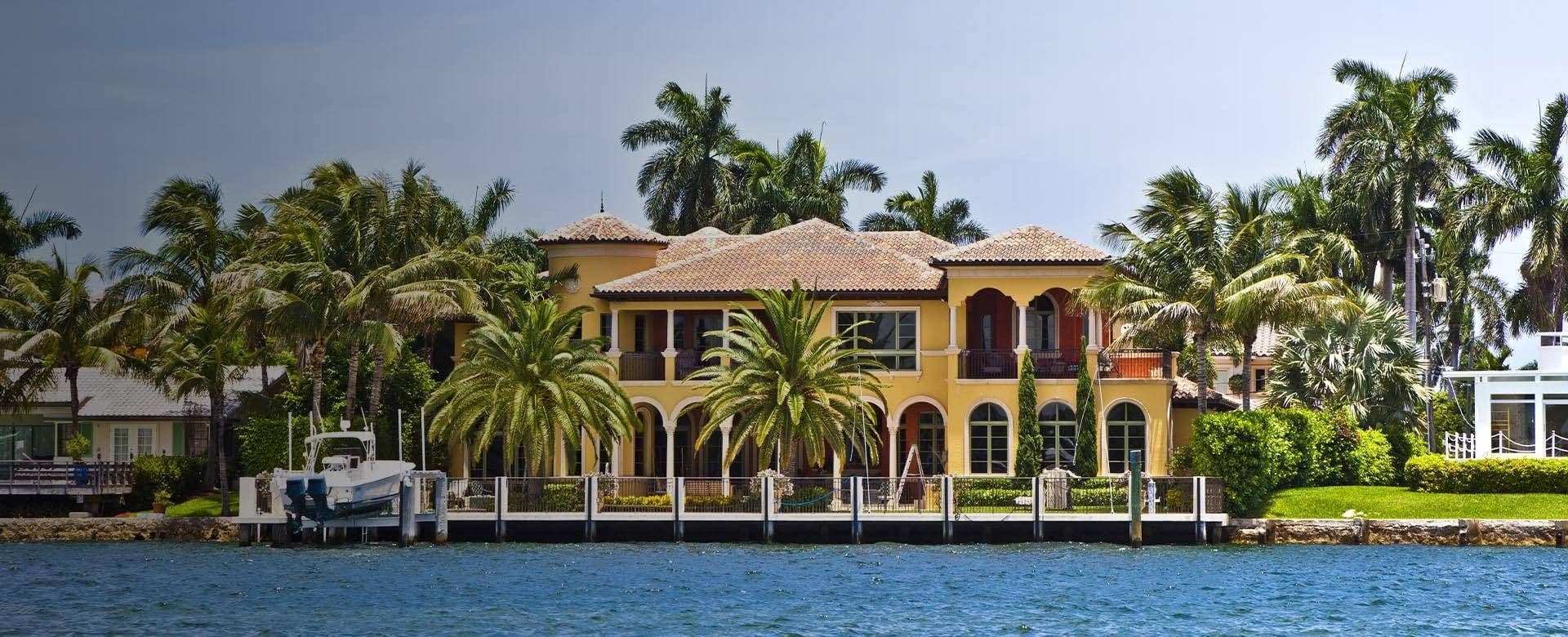 A large waterfront house surrounded by palm trees, showcasing a tropical and serene environment.