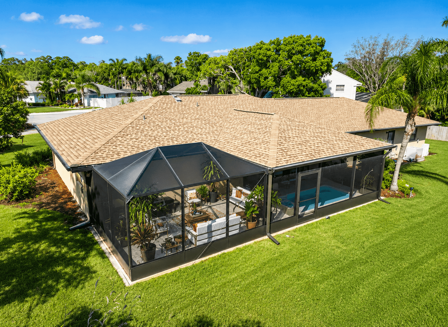 Aerial view of a single-story Florida home with tan tile roof, black screened pool enclosure, and surrounding palm trees and green lawn.