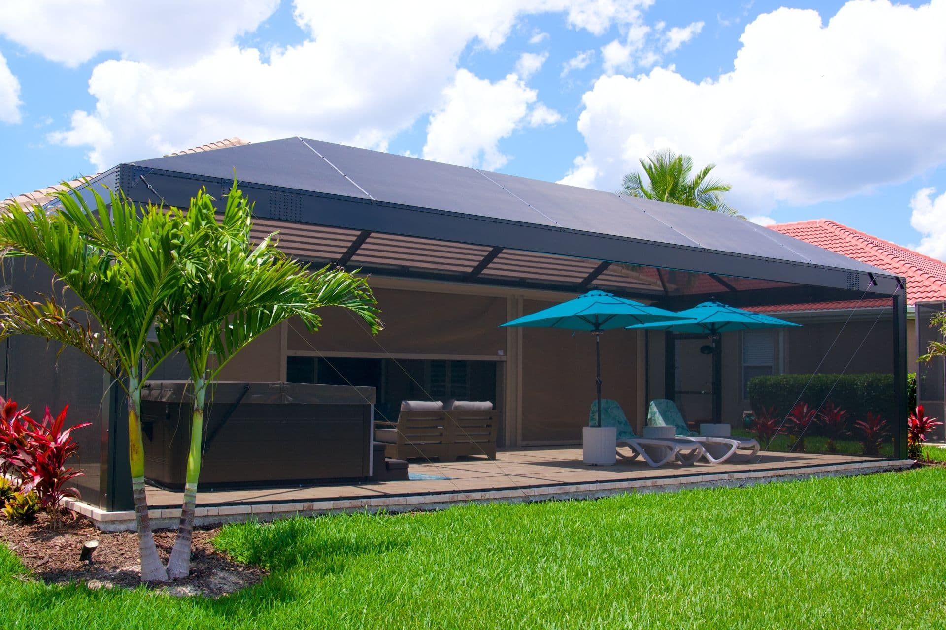 Modern tropical home with a screened patio, lounge chairs, turquoise umbrellas, palm trees, vivid lawn, and bright blue sky.