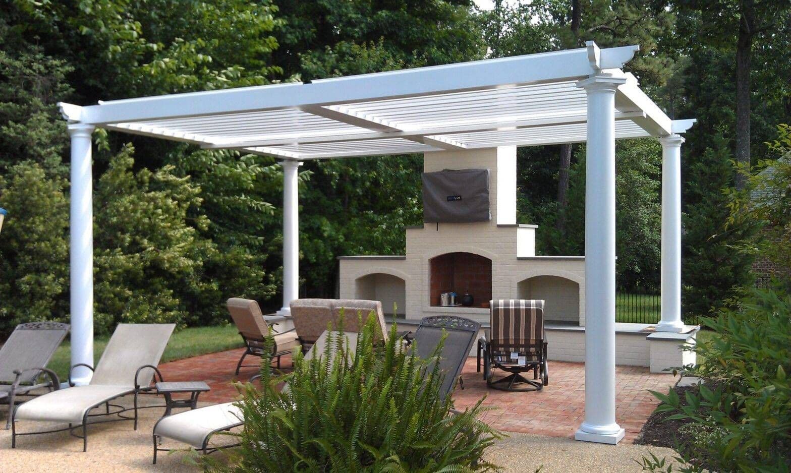 Outdoor patio with a white pergola, fireplace, lounge chairs, dining furniture, and lush greenery, creating a serene backyard retreat.