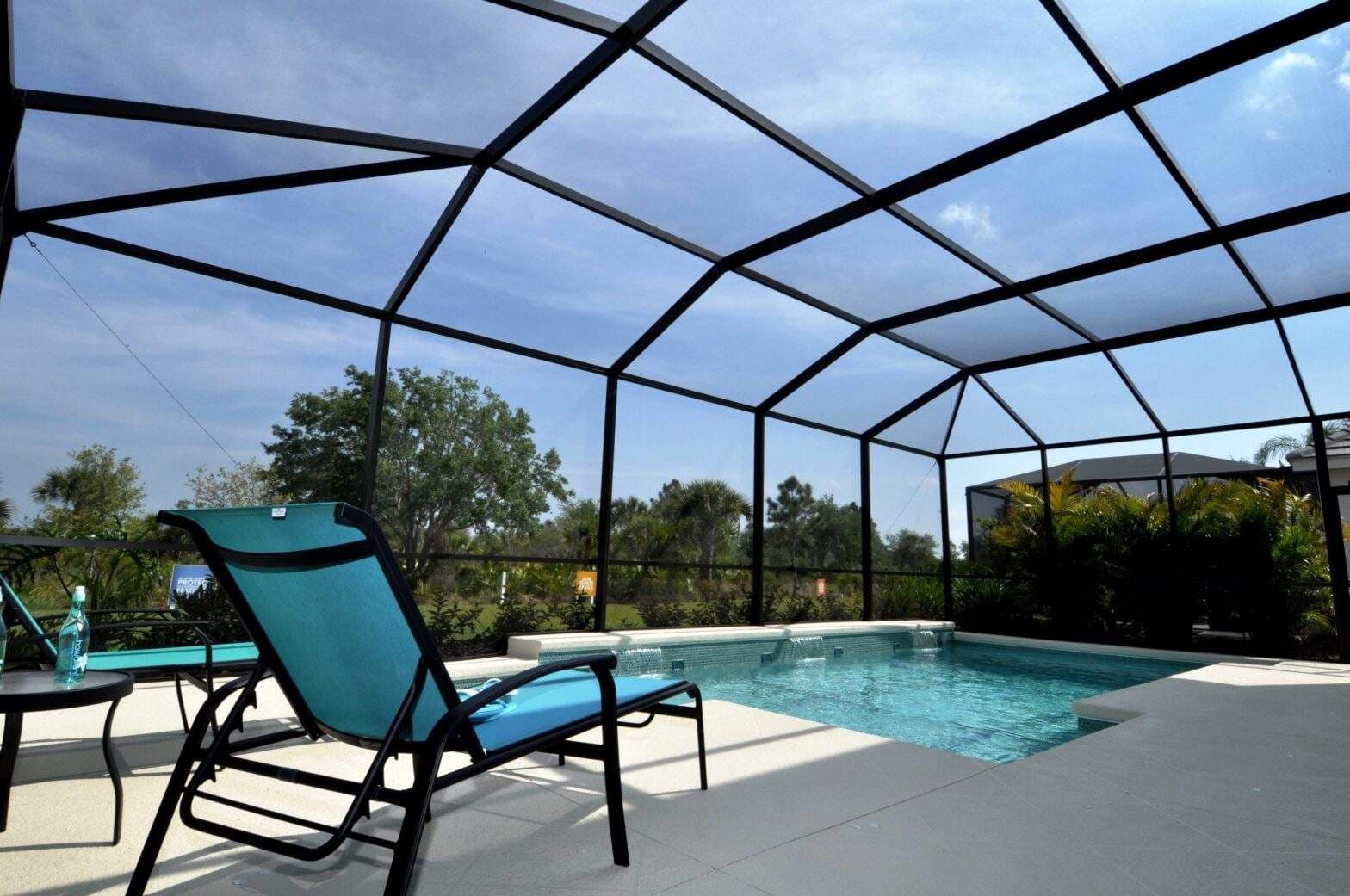 Sunlit screened-in backyard pool with turquoise water, lounge chairs, patio, and lush greenery creates a peaceful, inviting retreat.