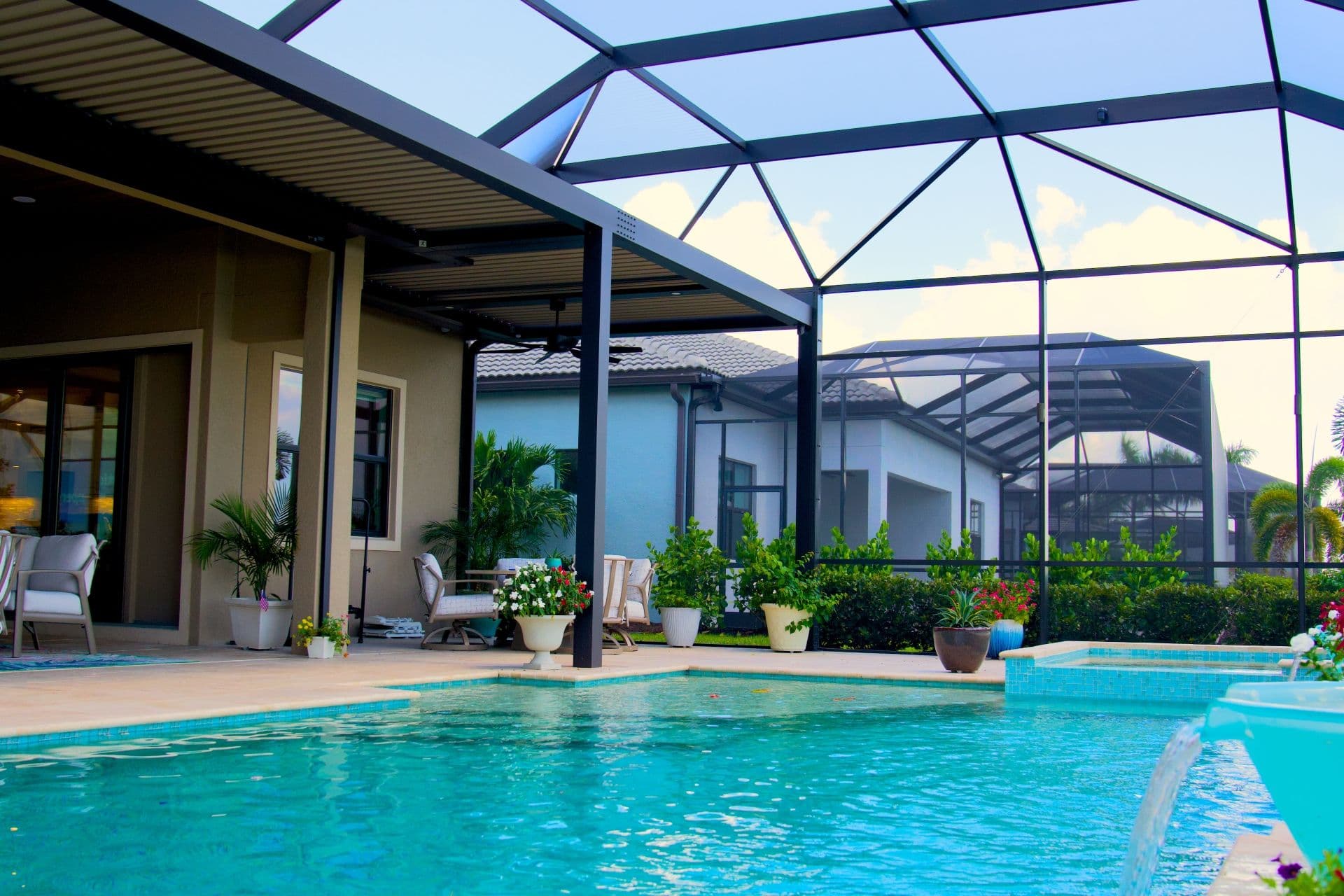 Bright outdoor pool patio with turquoise water, screened enclosure, modern home, potted plants, and lounge seating in a serene setting.