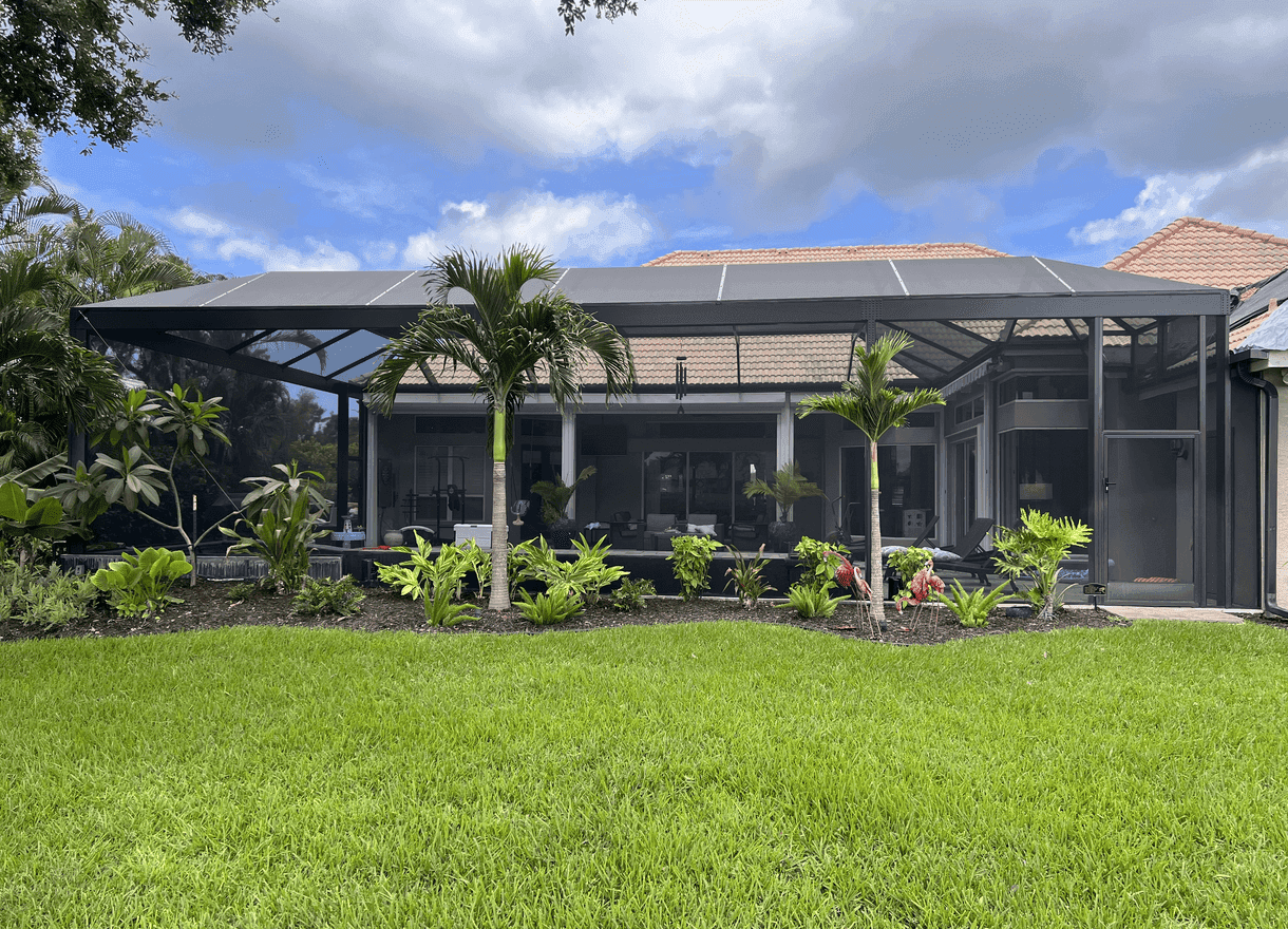 Contemporary tropical home with a screened patio, lush palms and garden, broad green lawn, and blue skies with clouds; serene and inviting.