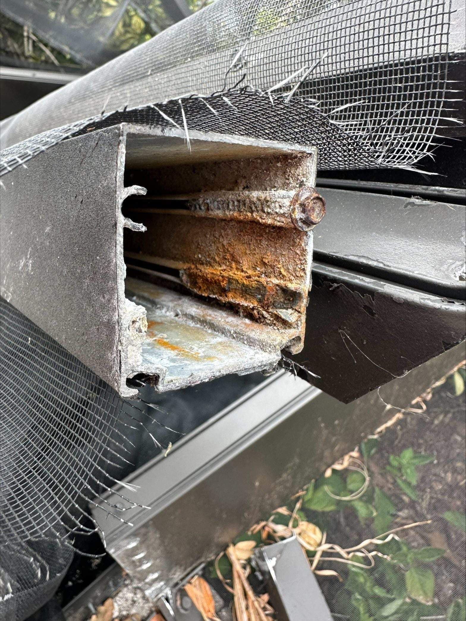 Close-up of a severely rusted rectangular metal beam exposed through torn black mesh, showing corroded layers and damaged outdoor equipment.