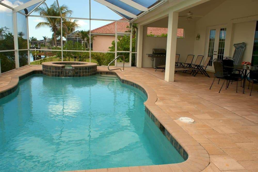 Sunlit backyard swimming pool with raised spa, screened patio, palm trees, lounge chairs, and tropical greenery creating a relaxing resort-like setting.